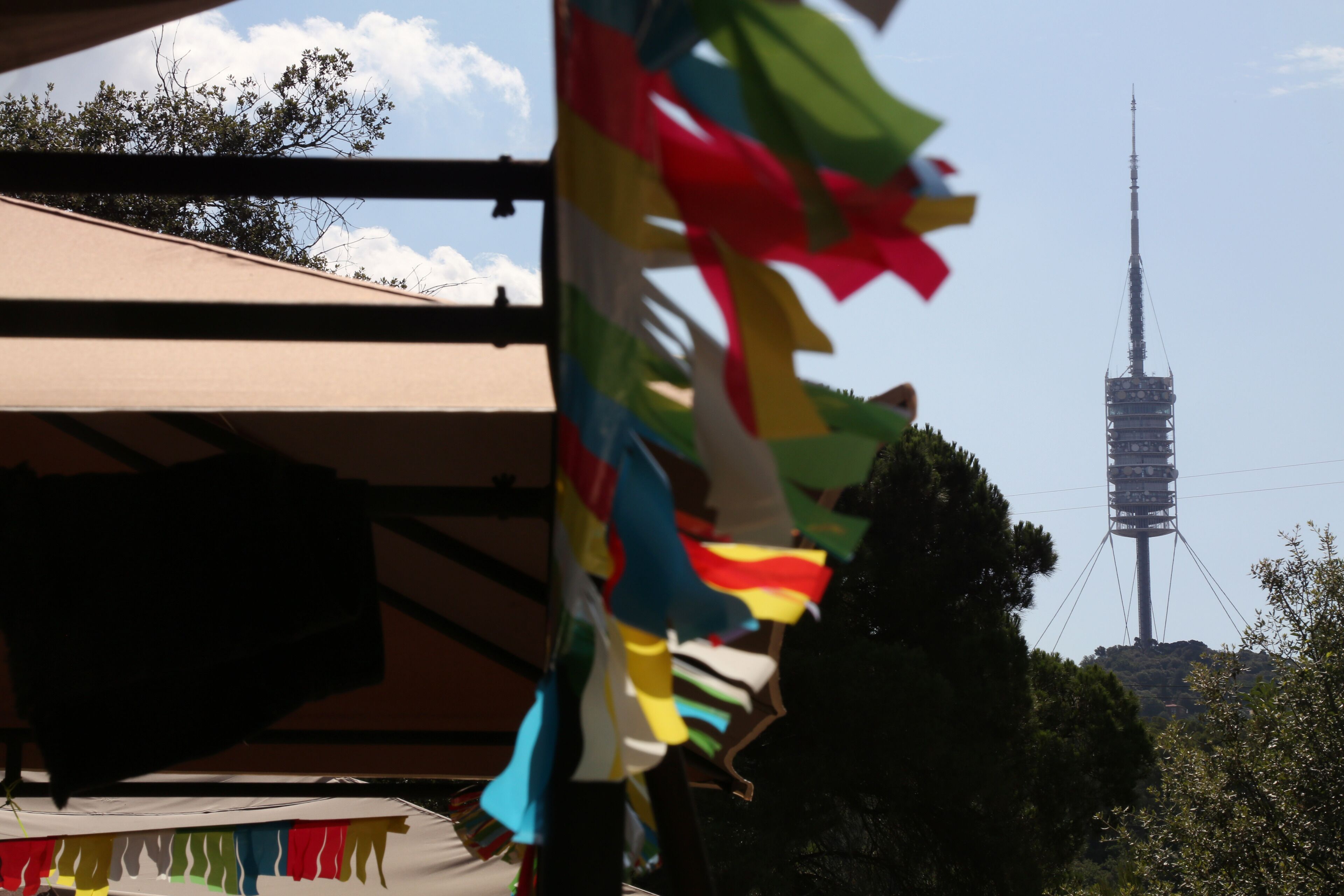 Un mât sur lequel flottent des drapeaux aux couleurs vives, un ciel dégagé et, au loin, une haute tour de communication.