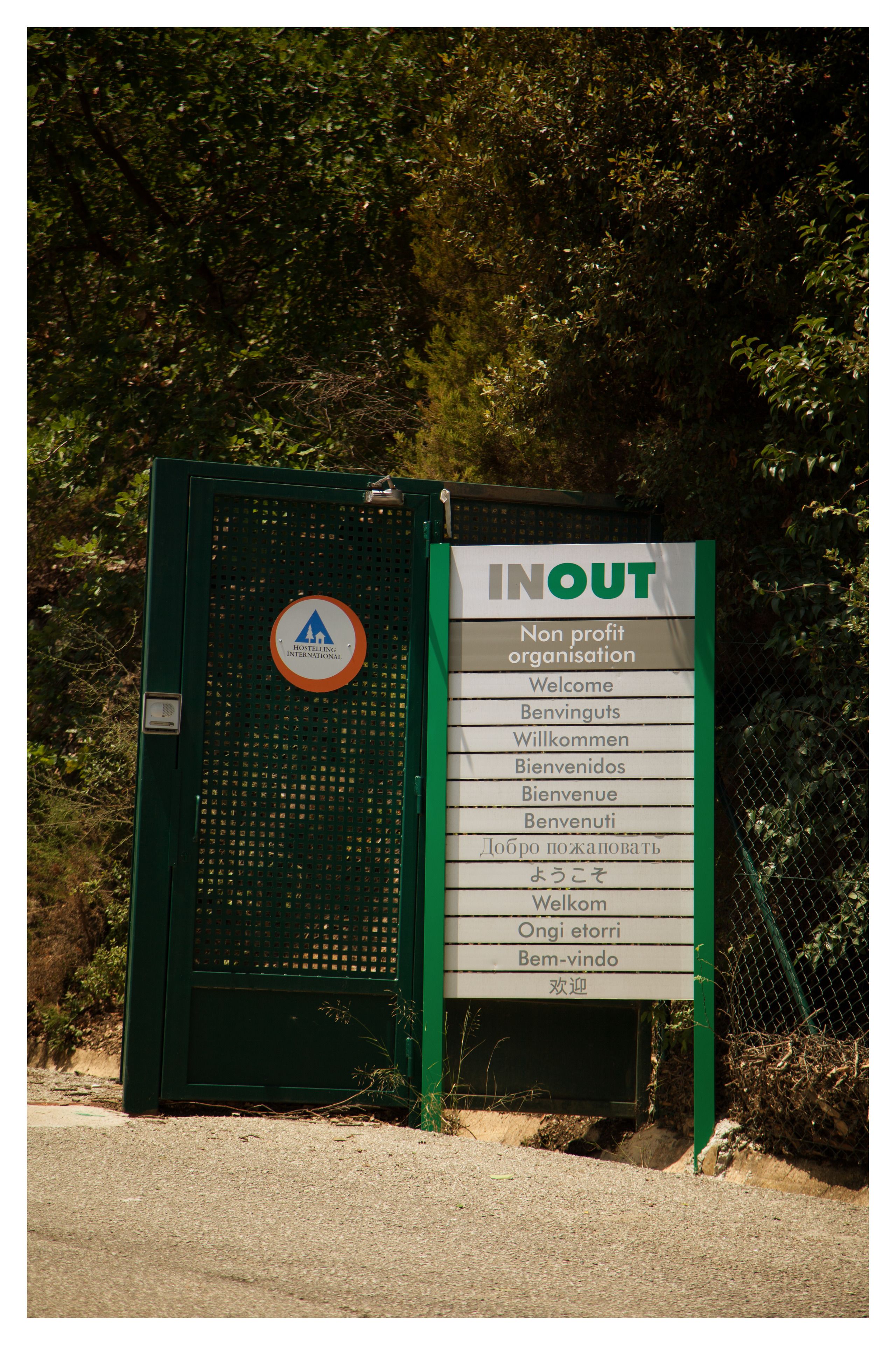 Una reja metálica verde con un letrero que enumera diversas frases de bienvenida en varios idiomas.