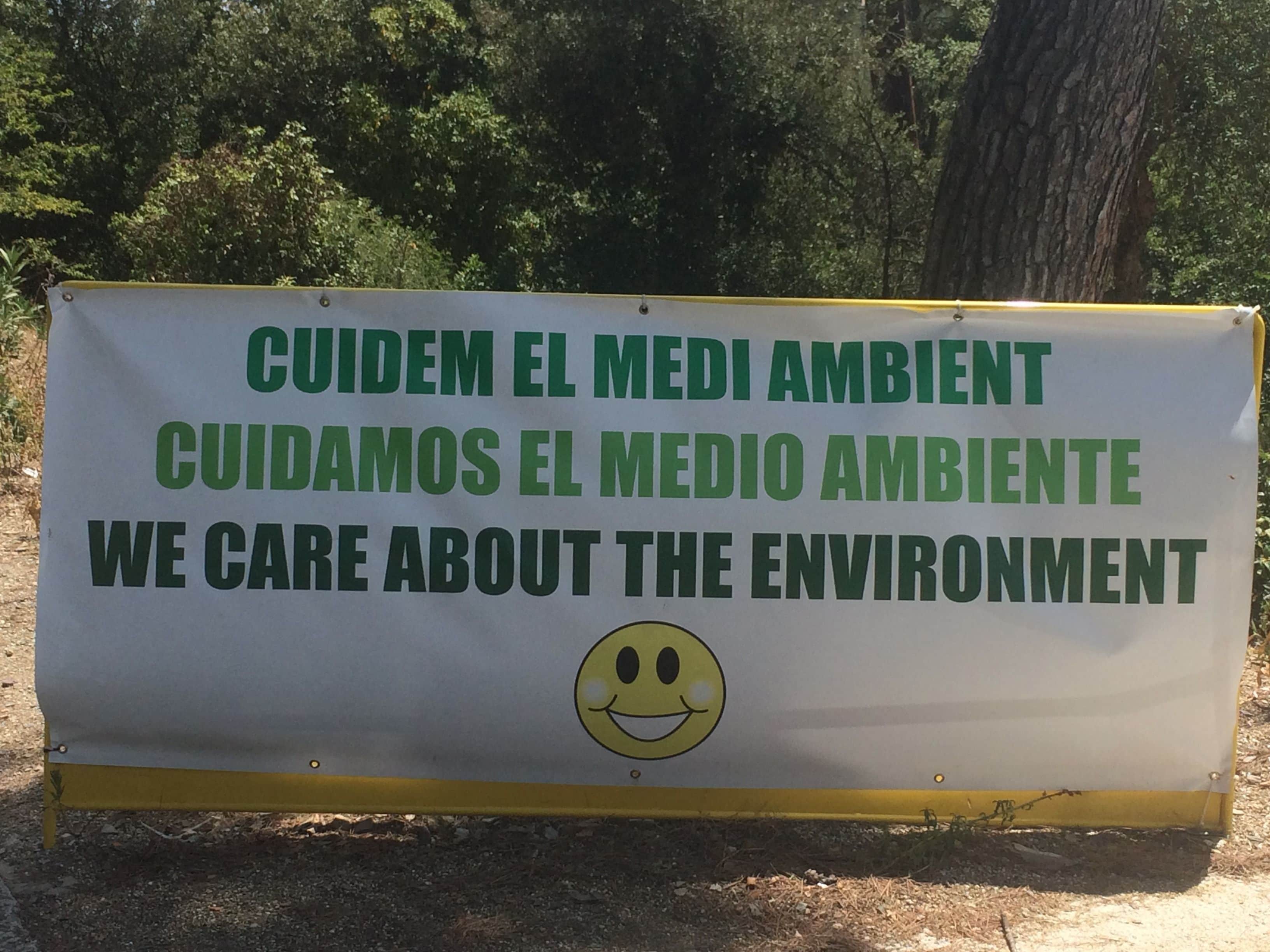 A sign with a smiley face, stating "CUIDEM EL MEDIO AMBIENTE" and "WE CARE ABOUT THE ENVIRONMENT".