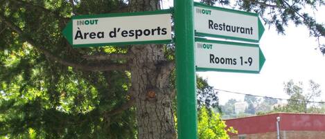 Un panneau indicateur avec les inscriptions « IN » et « OUT » pointant vers « Zone d’esports », « Restaurant » et « Chambres 1 à 9 ».