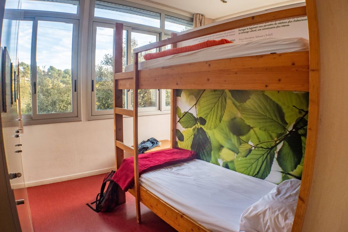 A bunk bed with a leaf-patterned headboard, a red blanket, and a backpack on the floor.