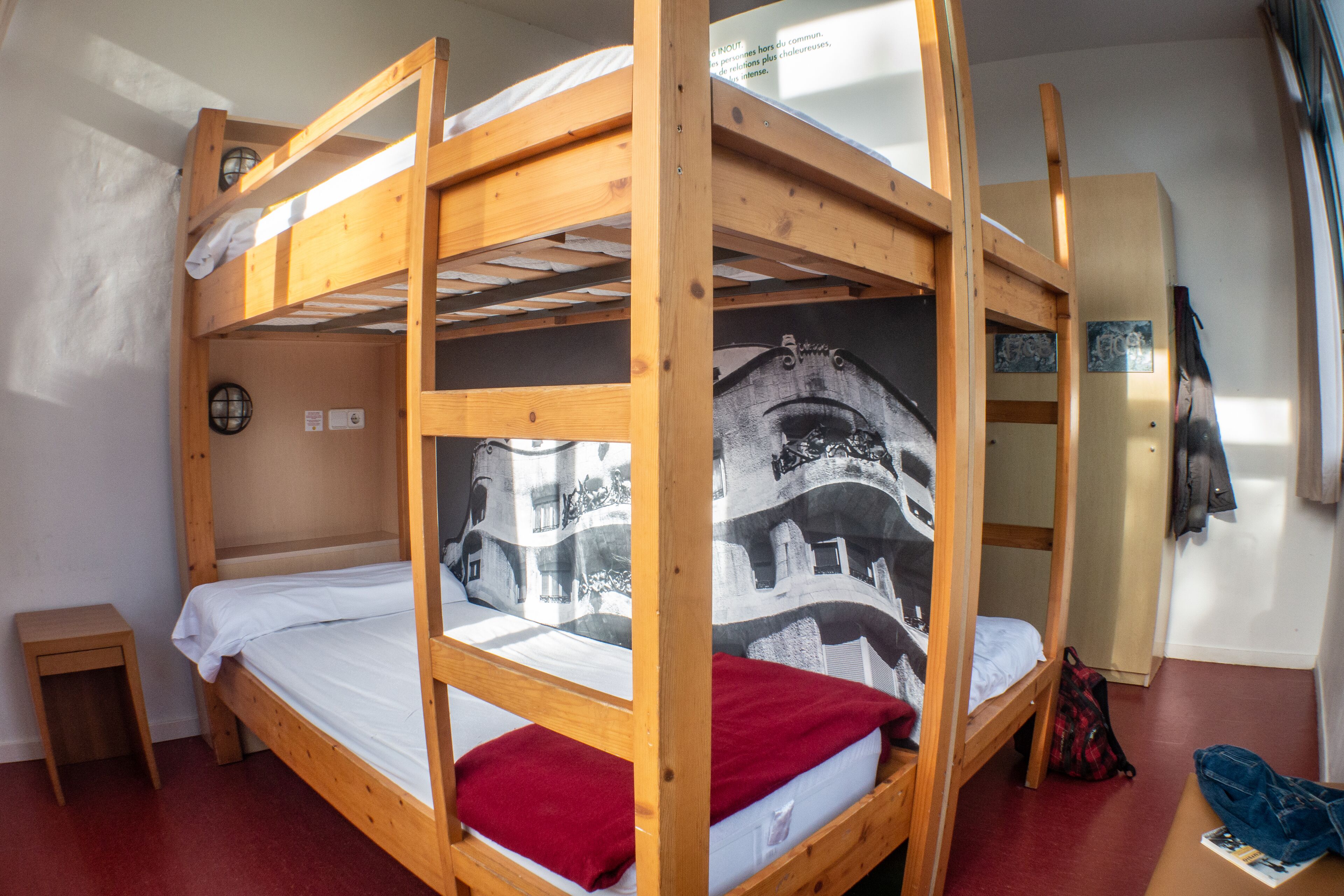 Ein Schlafraum mit Etagenbetten, einer kleinen Holz-Nachttisch und einer Wand mit einem schwarz-weißen Stadtbild-Wandgemälde.