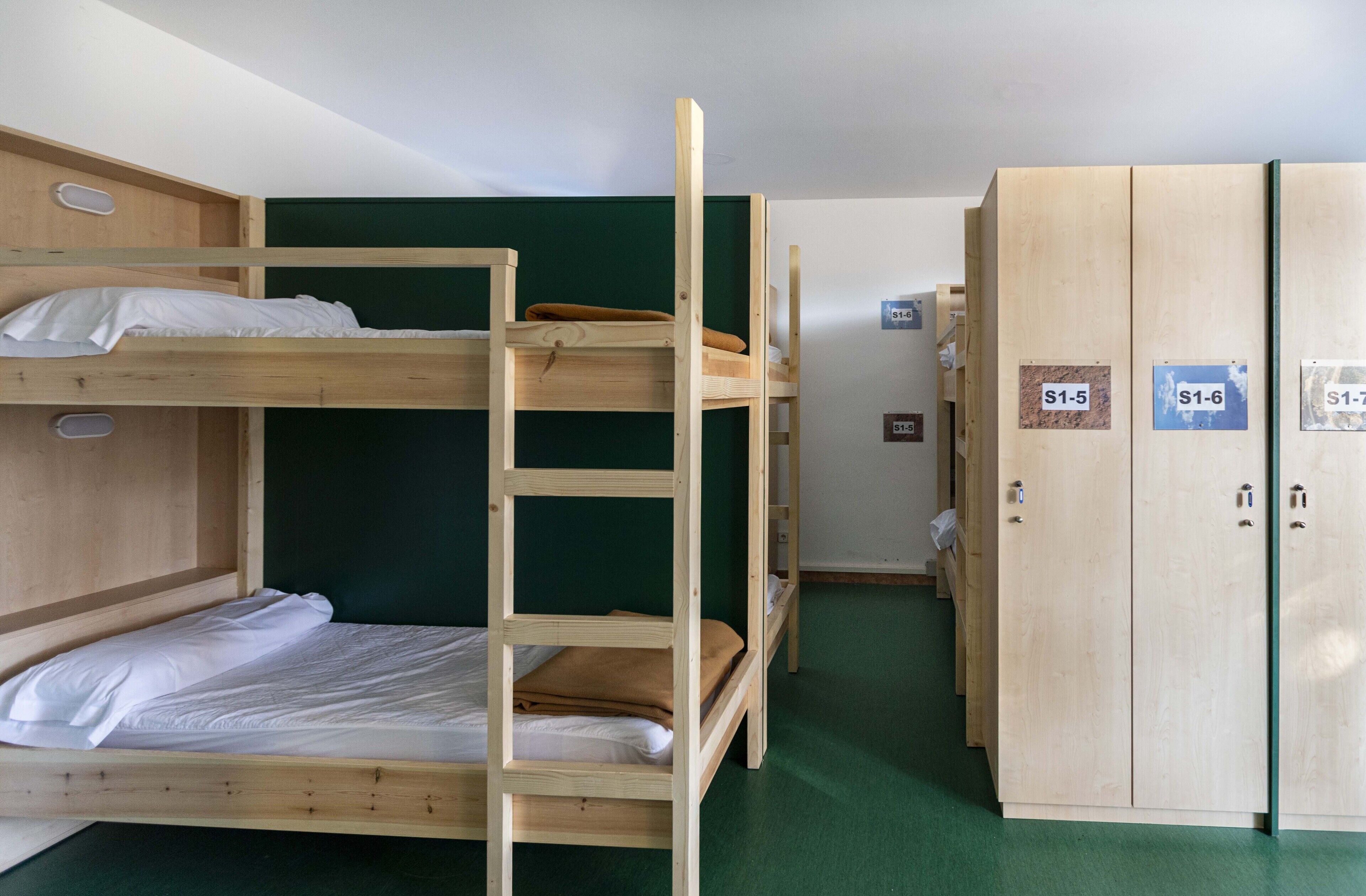 Une chambre avec un lit superposé, un mur vert, une armoire en bois et une moquette verte.