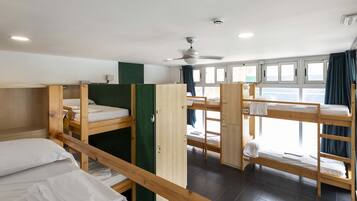 Een slaapzaal met stapelbedden, een plafondventilator en een raam met gordijnen.