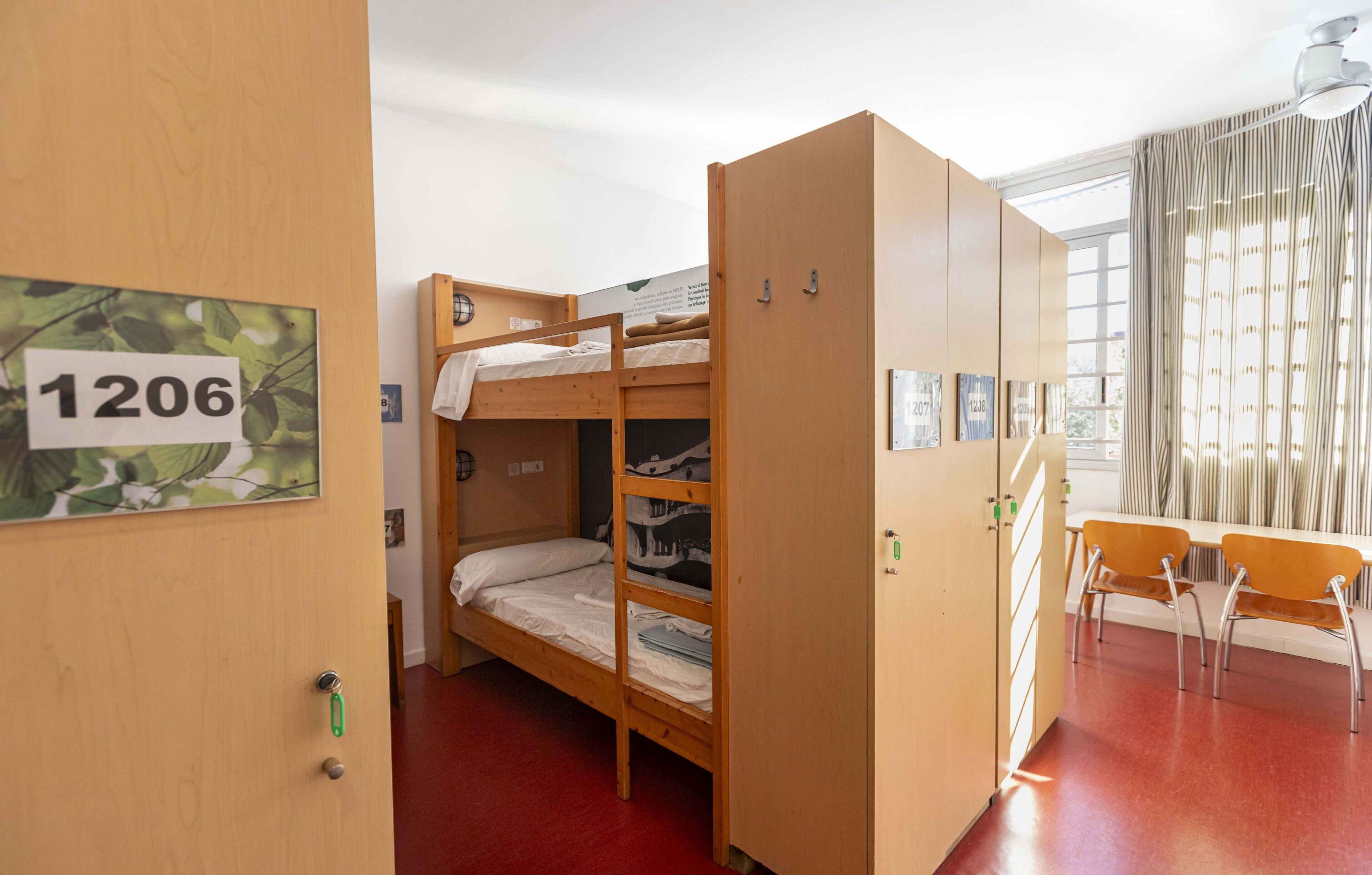 Habitación con literas, un letrero con número, escritorio, sillas y ventana con cortinas.