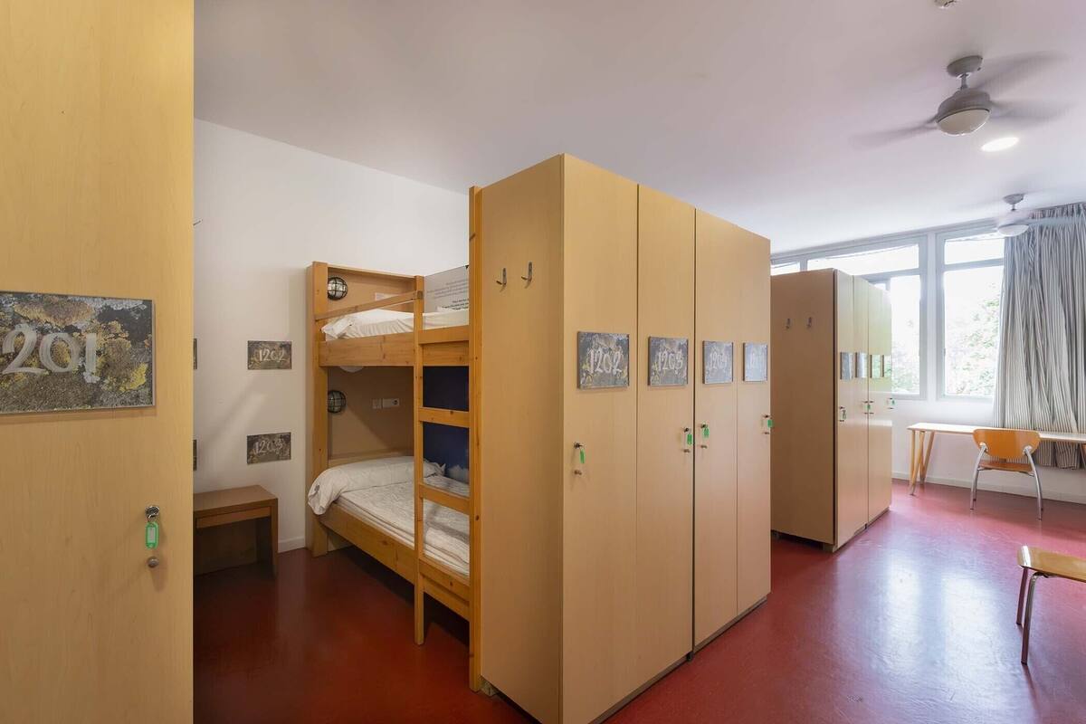 A dormitory room with bunk beds, a wardrobe, a desk, and a chair.