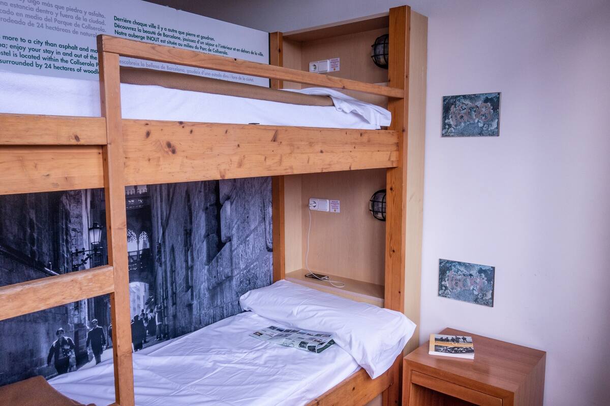 A bunk bed room with a wooden frame, a white mattress, and a small wooden nightstand with a book.