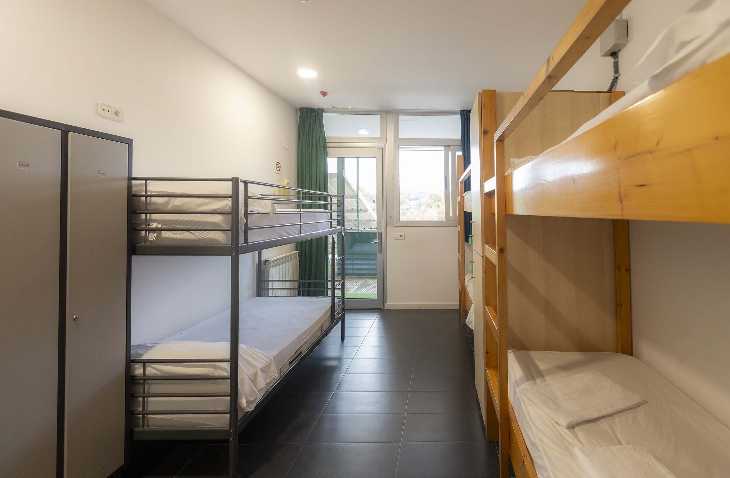 A dormitory room with bunk beds, a wardrobe, and a window with a view.