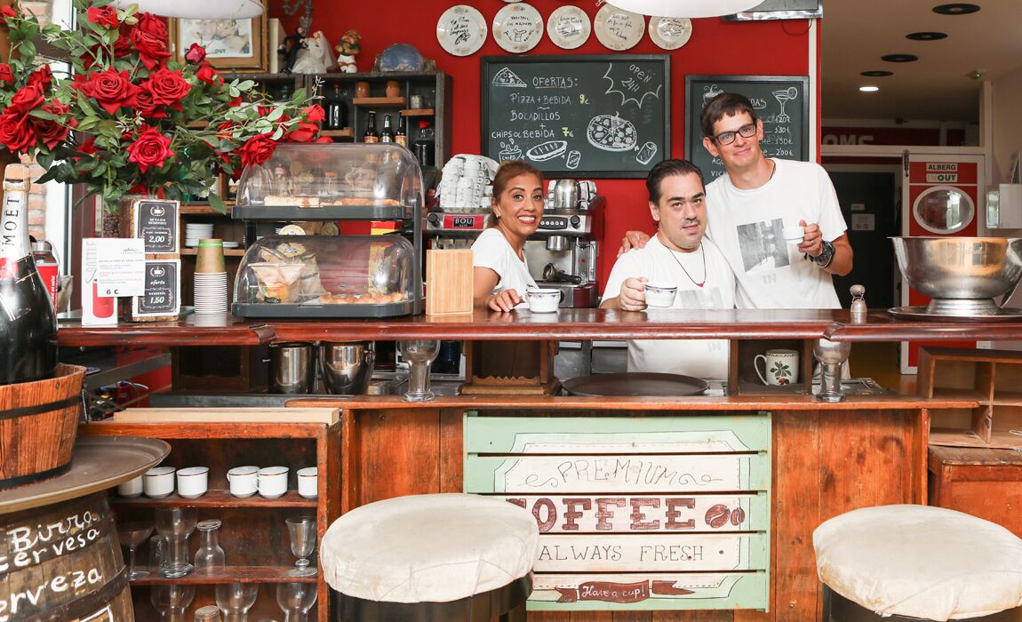 A coffee shop counter with a menu board, coffee brewing equipment, and a flower arrangement.