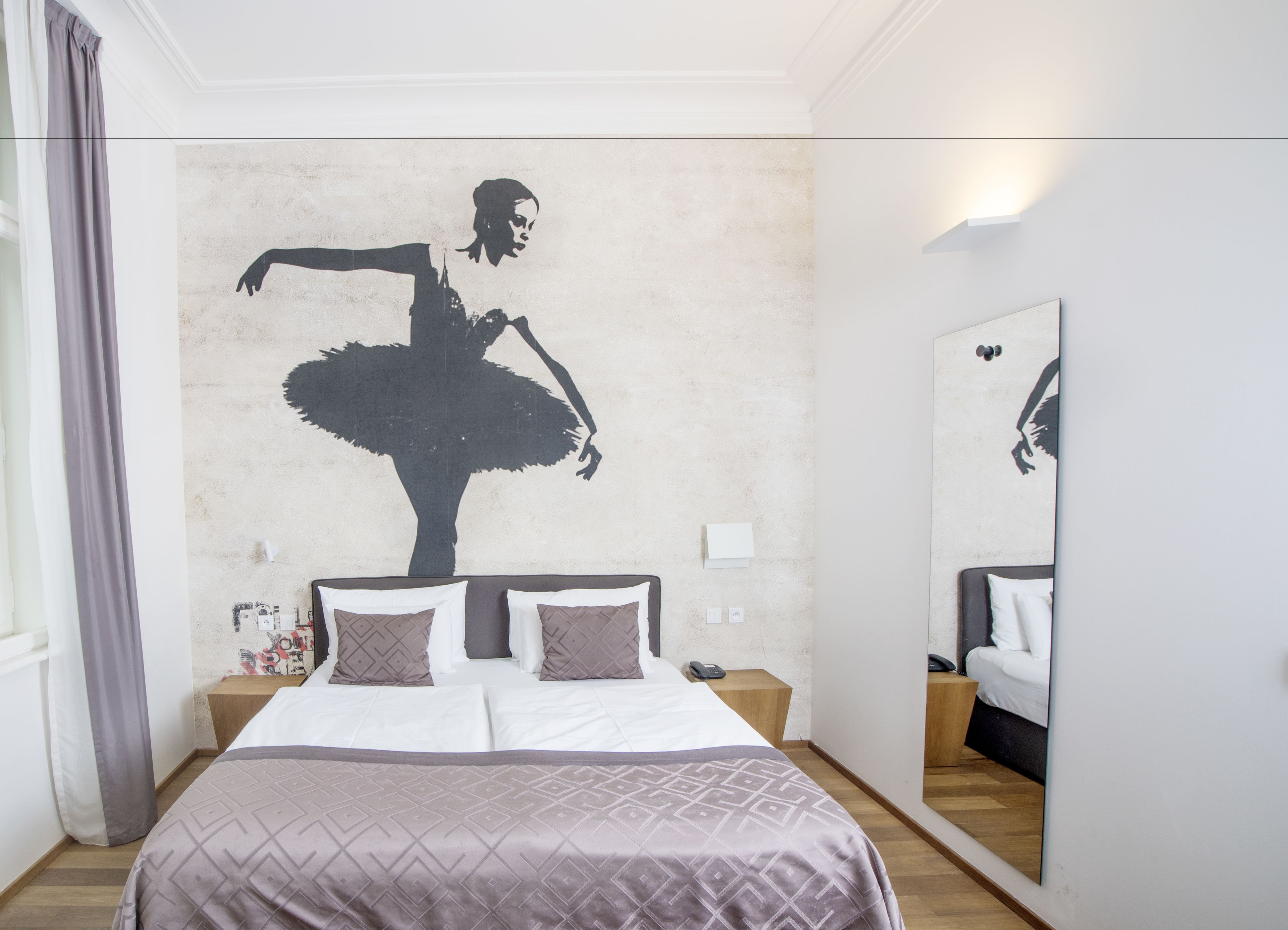 Une chambre avec un grand lit, un miroir et une fresque murale représentant une ballerine.