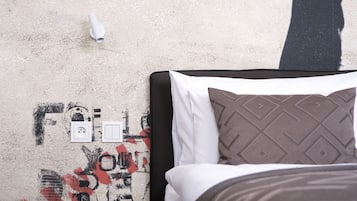 Un lit avec un oreiller à motifs, un mur blanc orné d’un dessin de style graffiti et une prise de courant.