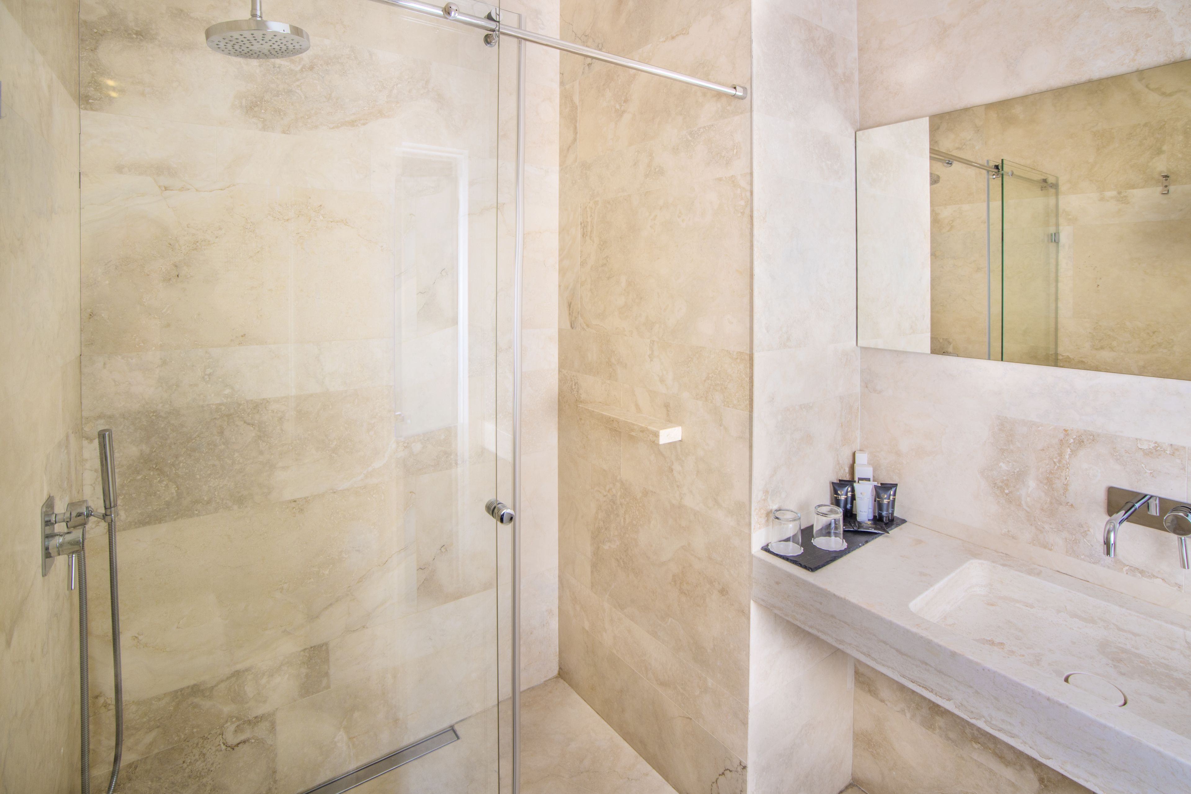 A modern bathroom with a glass-enclosed shower, a marble-tiled wall, and a sink with a mirror above it.