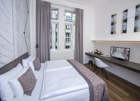 Quarto de hotel com uma cama, uma escrivaninha, uma cadeira, uma televisão e uma janela com cortinas.