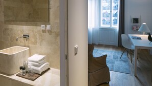A modern bathroom with a bathtub, a towel rack, and toiletries. It leads to a living area with a sofa, a table, and a lamp. - Golden Crown (Prague)