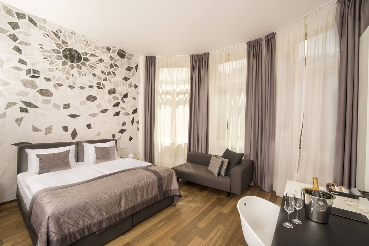 Una habitación de hotel moderna con una cama grande, un sofá, una mesita con una botella de champán y una decoración de pared.