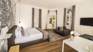 A modern hotel room with a large bed, a sofa, a desk with a TV, and a view of the outside. - Golden Crown (Prague)