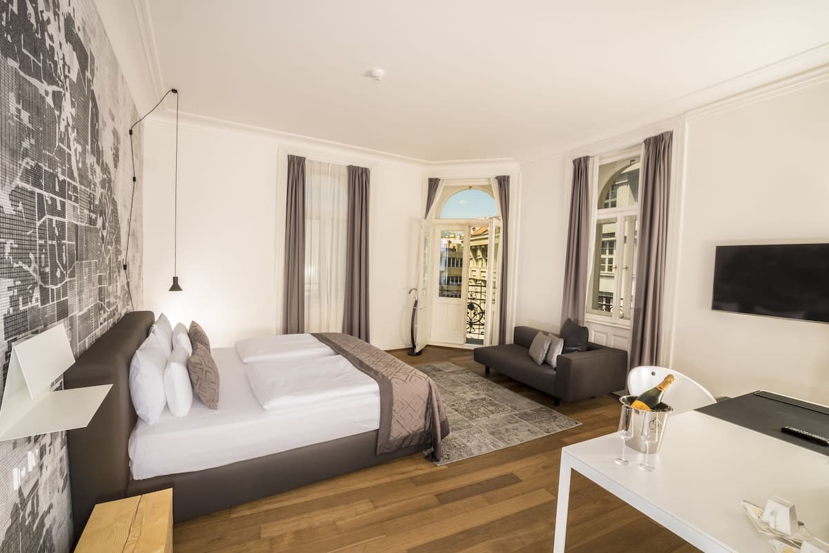 Una habitación de hotel moderna con una cama grande, un sofá, un escritorio con televisor y vistas al exterior.