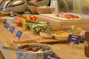 Buffet com diversas opções de comida, incluindo quiche de salmão, saladas e carnes.