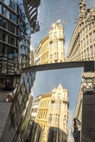 Um edifício moderno com fachada de vidro e, ao fundo, um edifício clássico com detalhes ornamentados.
