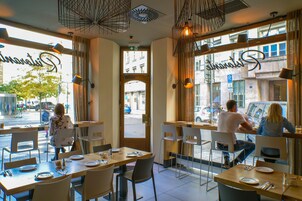Um restaurante com mesas e cadeiras, uma placa com o nome 'Shamrat' e vista para a rua.