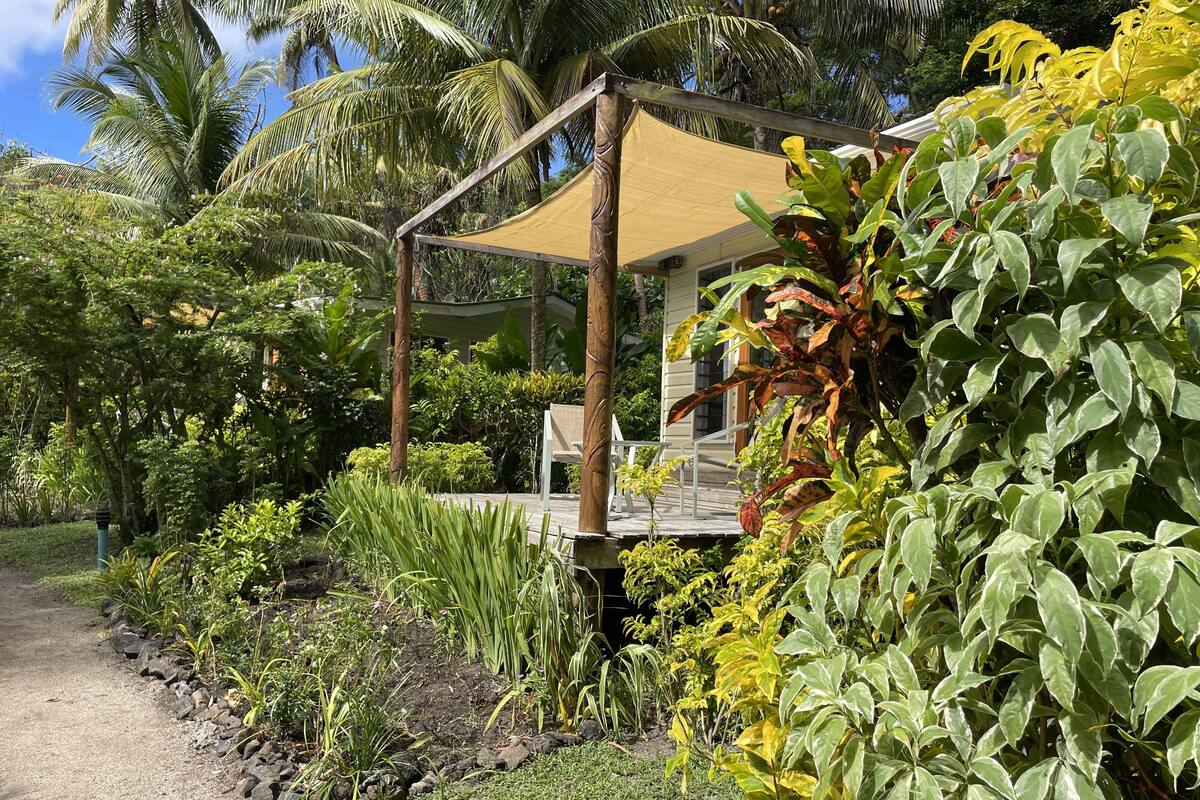 Ein überdachter Außenbereich mit Holzdeck, umgeben von üppiger tropischer Vegetation und Palmen.