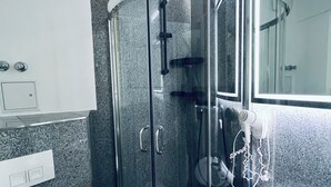 Un baño moderno con cabina de ducha de vidrio, un lavamanos blanco y un espejo grande.