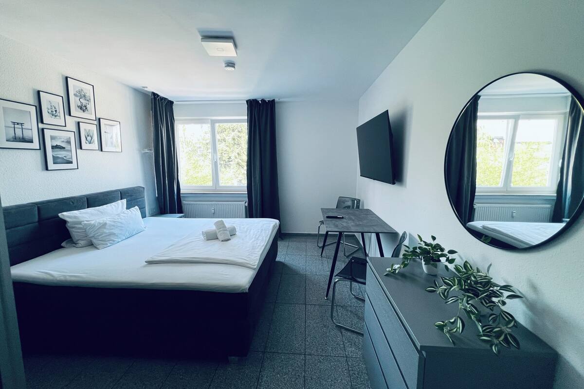A hotel room with a bed, a desk, a TV, and a window with curtains.
