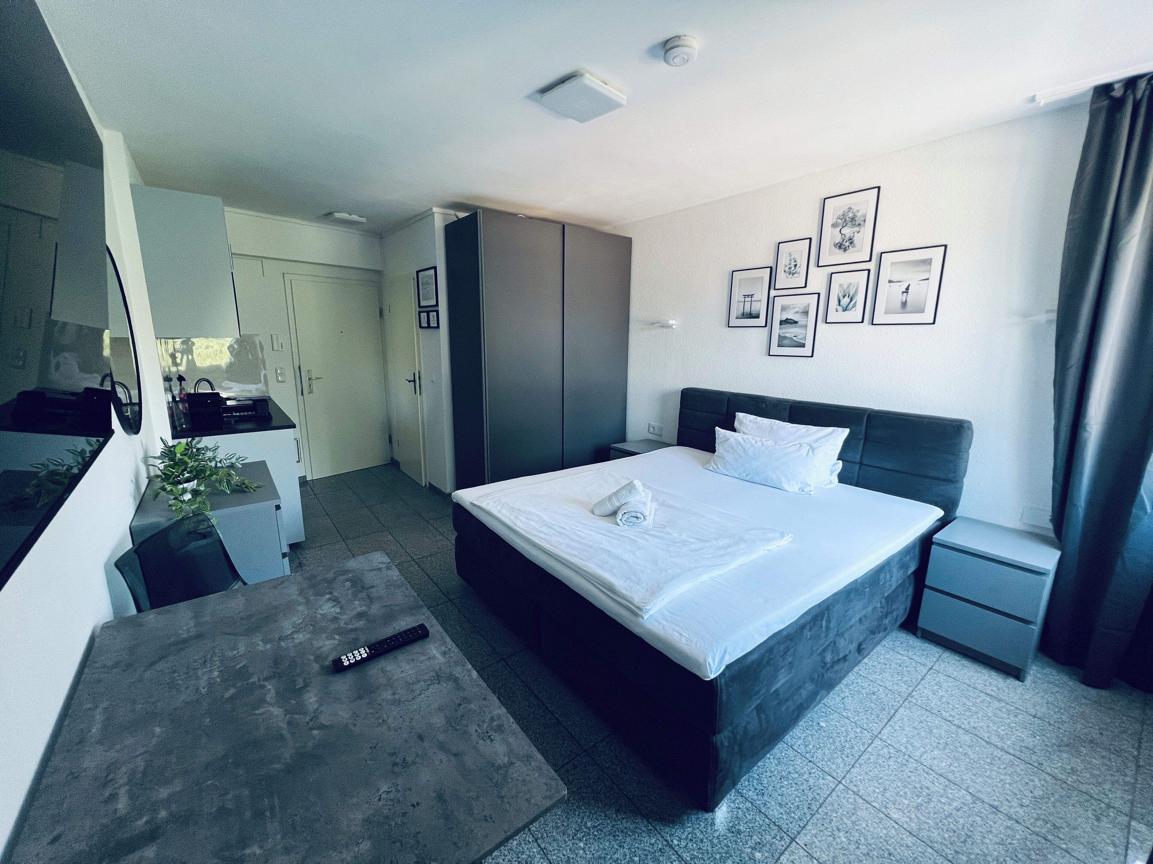 A modern hotel room with a large bed, a desk, and a wardrobe.