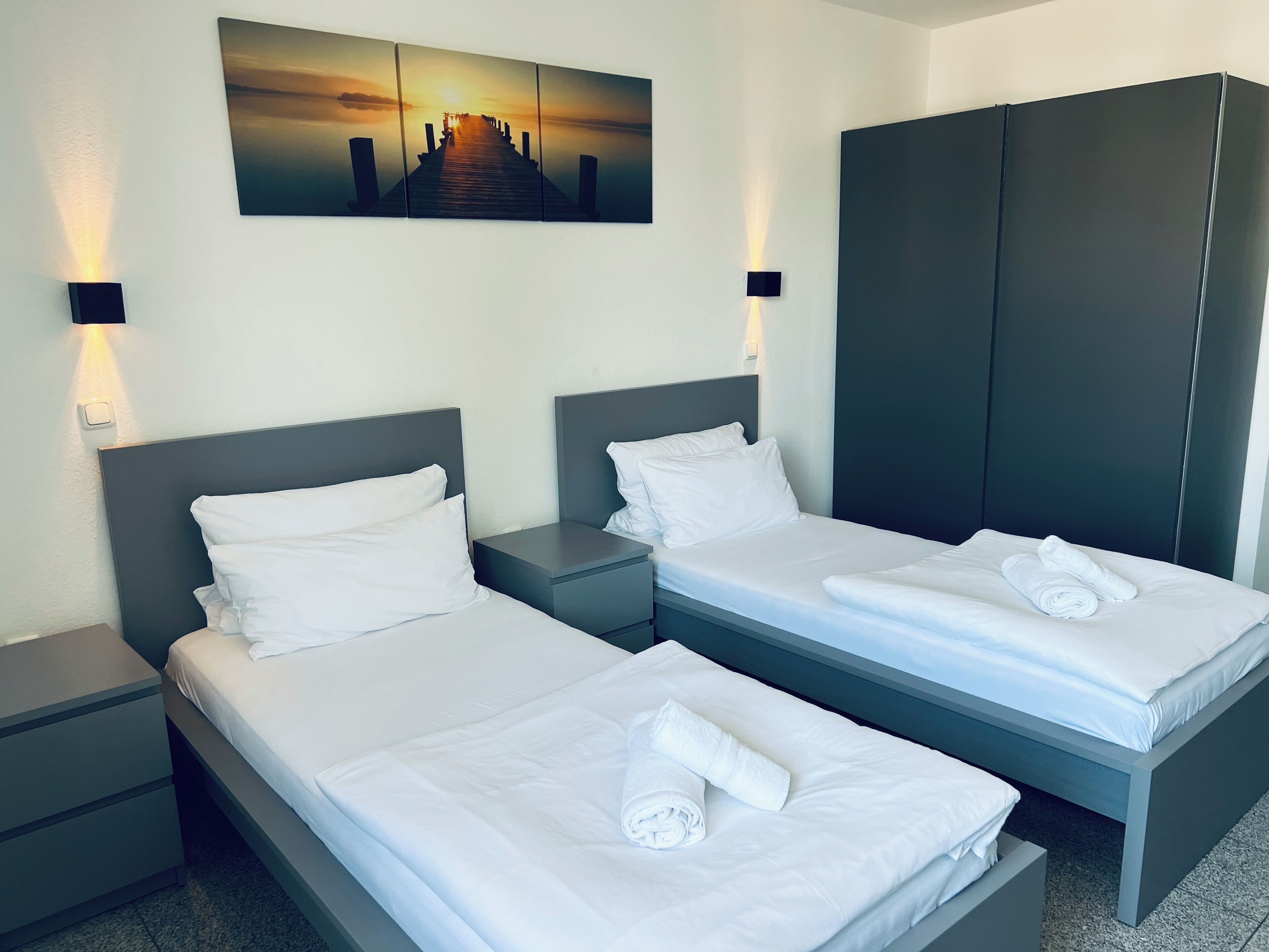 Ein Hotelzimmer mit zwei Betten, einem großen Kleiderschrank und einem Gemälde mit Sonnenuntergang an der Wand.