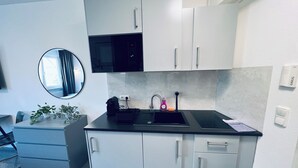 Una cocina moderna con armarios blancos, una encimera negra, un microondas, un lavamanos con grifo y una pequeña planta en la encimera.