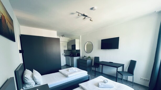 Una habitación de hotel moderna con dos camas, un escritorio, una silla, un televisor y una kitchenette.