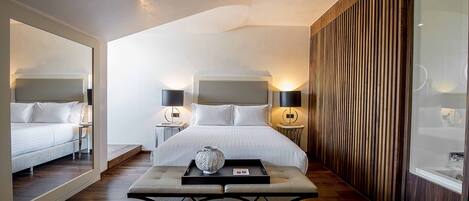 A modern hotel room with a large bed, two bedside tables with lamps, a small table with a vase, and a wooden accent wall.