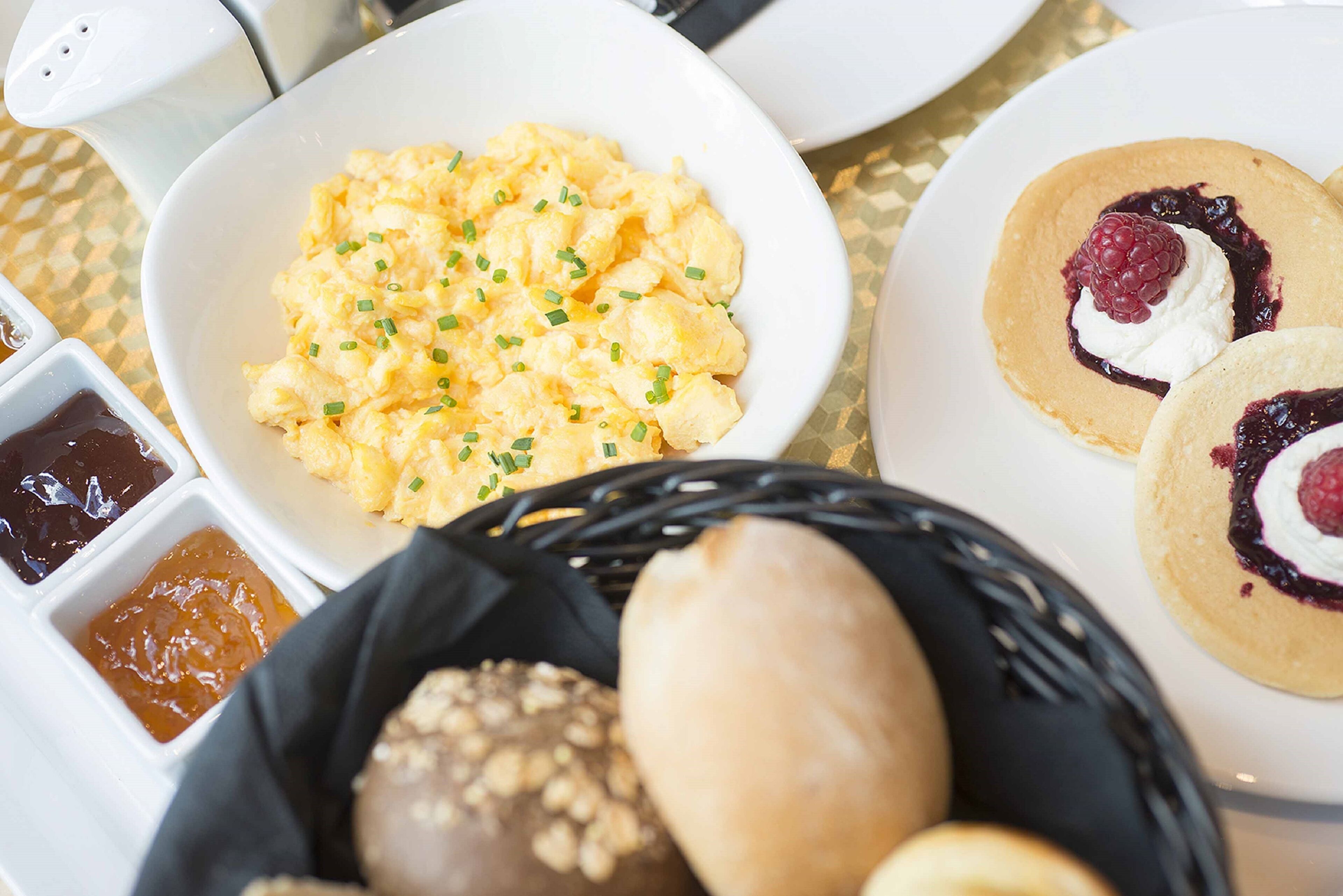 A breakfast setting with scrambled eggs, pancakes with berries, and bread.