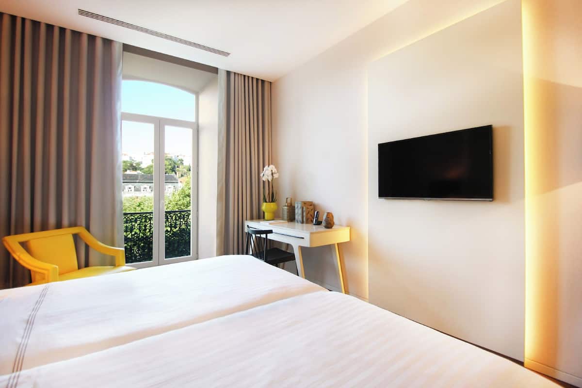 A hotel room with a bed, a desk, a chair, a TV, and a window with curtains.