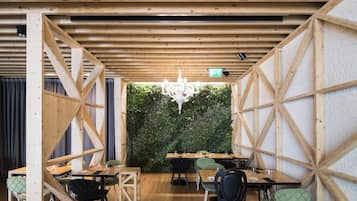A restaurant with wooden beams, a green wall, and a chandelier. Tables and chairs are arranged for dining.