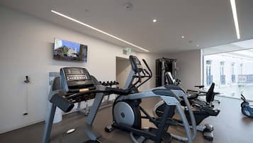 Un gimnasio con cintas de correr, elípticas y un televisor en la pared.