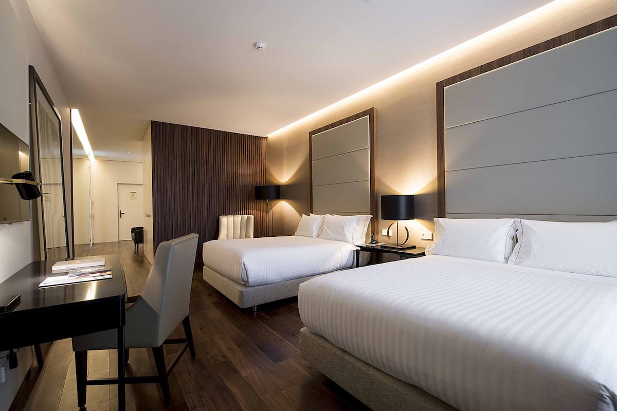 A modern hotel room with two beds, a desk, and a large mirror.
