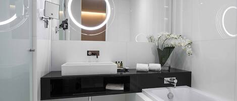 Un baño moderno con lavamanos blanco, tocador negro y bañera independiente.
