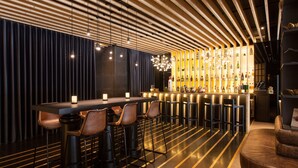 A modern bar area with a long counter, multiple stools, and a decorative light fixture above. - BessaHotel Liberdade (Lisbon)
