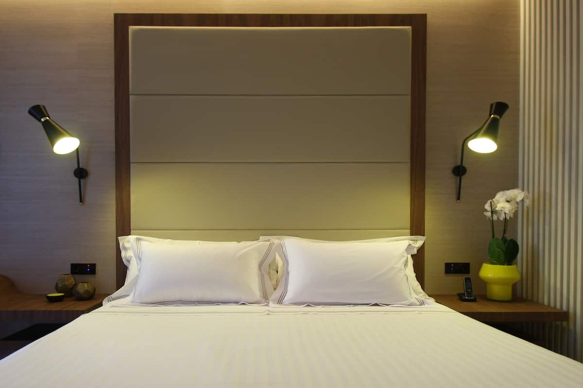 A neatly made bed with white linens, two bedside lamps, a vase with an orchid, and a small table with a remote control.