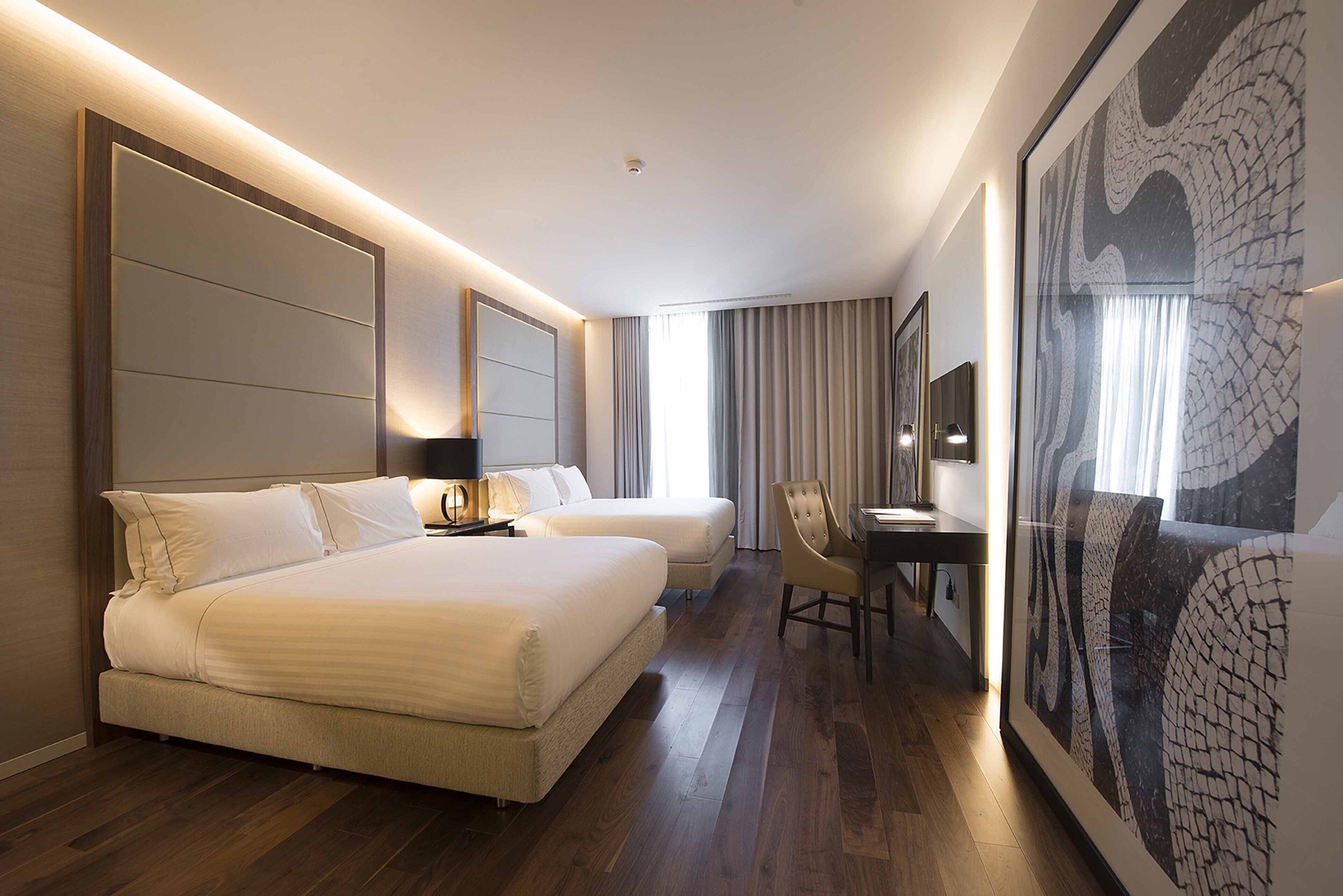 Habitación de hotel con una cama grande, un escritorio y una silla. Hay un cuadro grande en la pared y una ventana con cortinas.