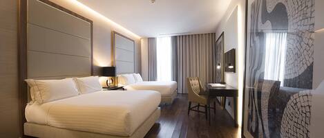 Habitación de hotel con una cama grande, un escritorio y una silla. Hay un cuadro grande en la pared y una ventana con cortinas.