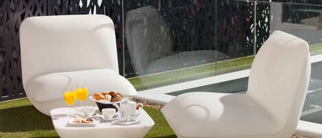 Two white chairs with a breakfast tray on a grassy area near a glass partition.