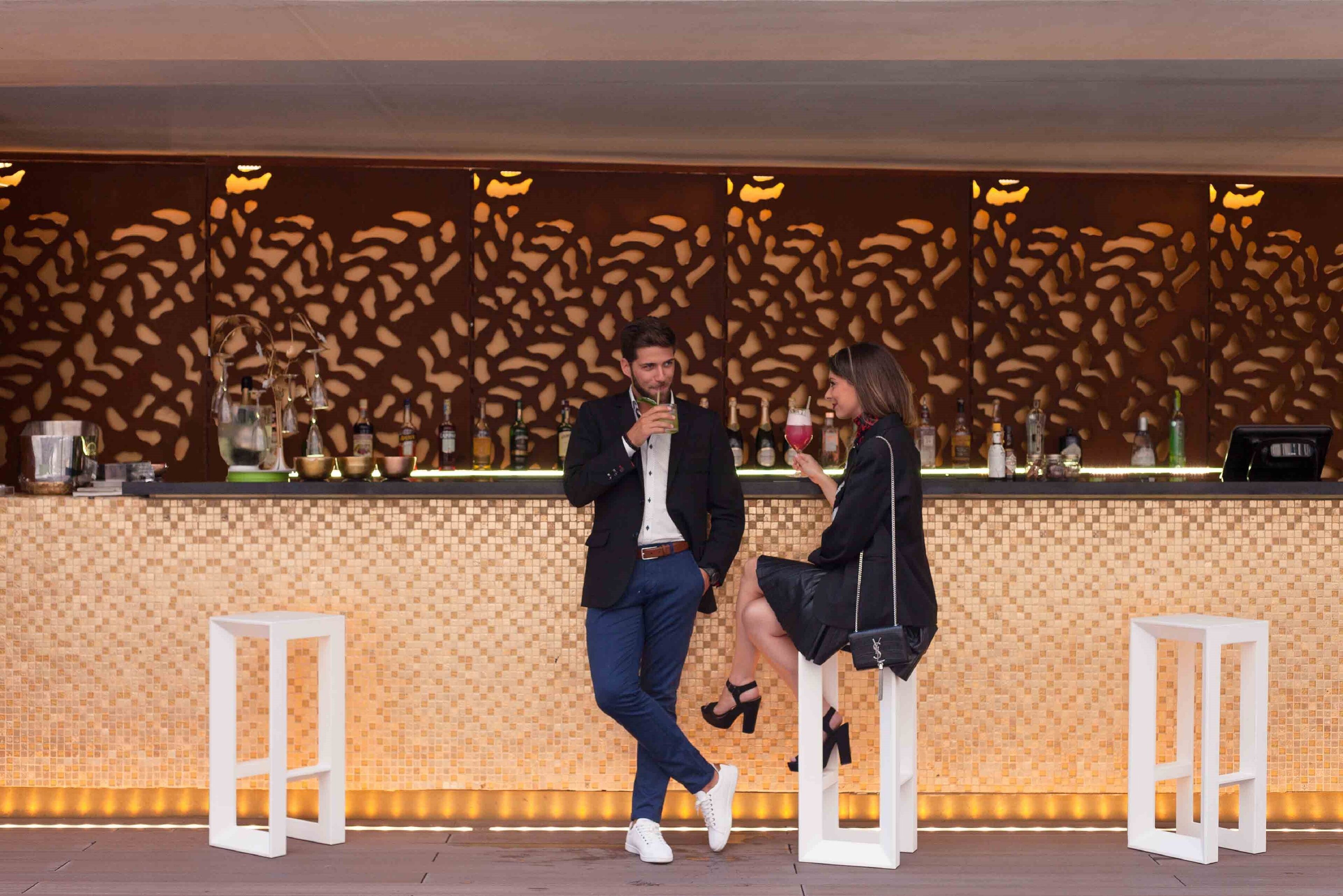 Uma área de bar com parede estampada, banquetas e um balcão com garrafas.