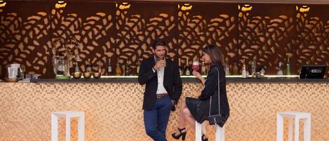 Uma área de bar com parede estampada, banquetas e um balcão com garrafas.