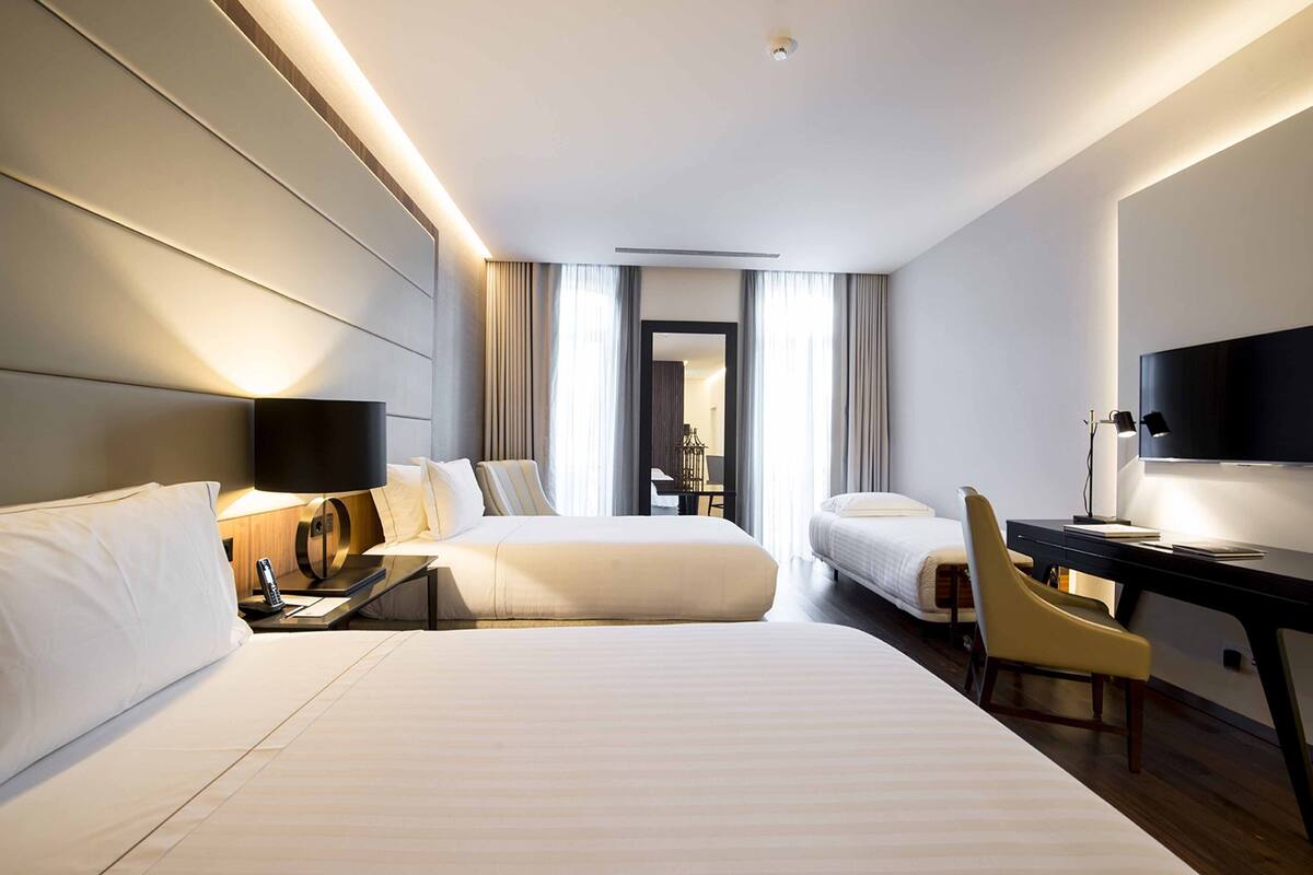 A modern hotel room with two beds, a desk, a chair, and a TV.