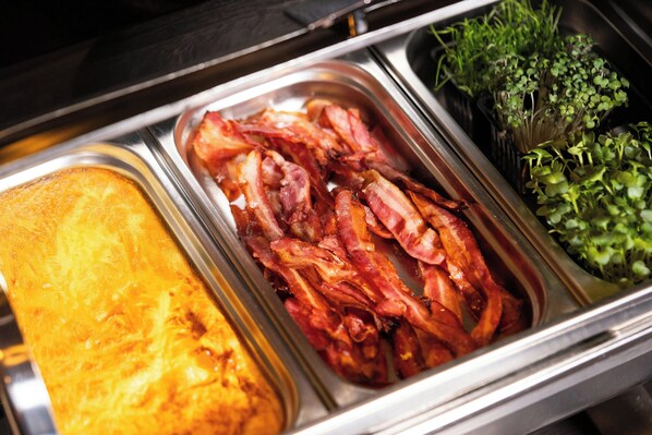 Un bufé con diversas opciones de comida, incluyendo tocino, un plato al horno y vegetales.