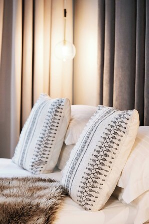Ein Bett mit zwei Kissen, einem Fellüberwurf und einer hängenden Leuchte mit geometrischem Muster.