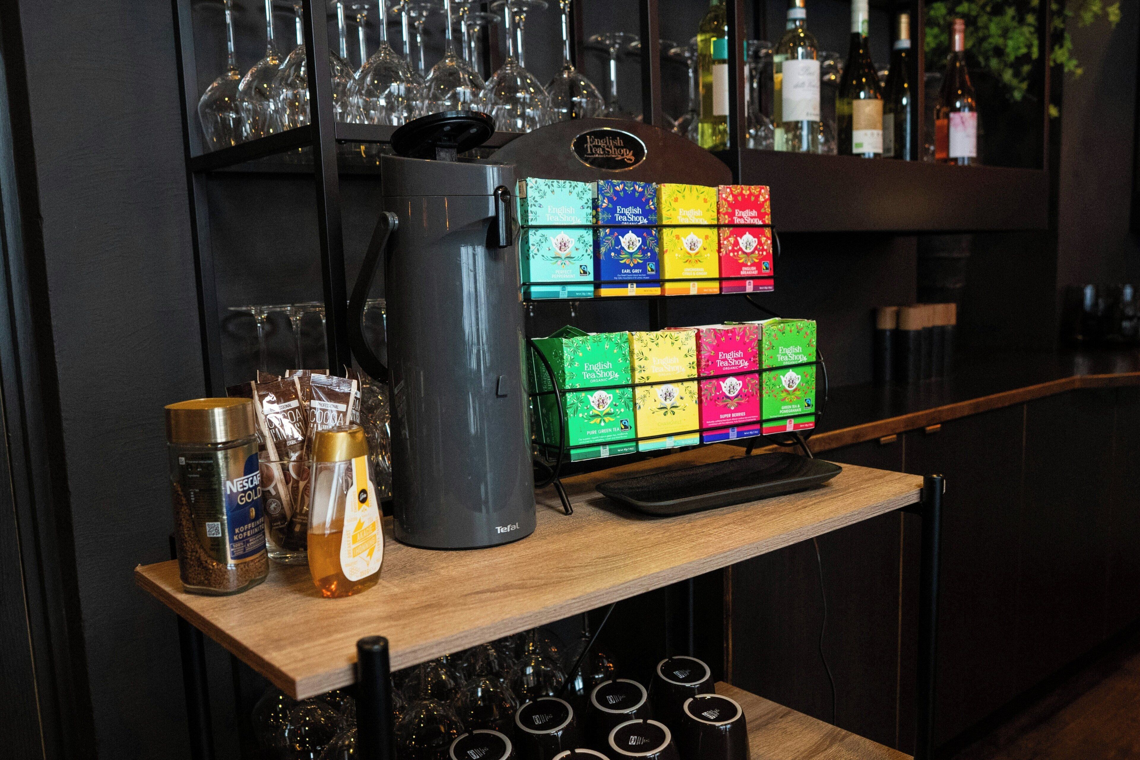 Una cafetera, cajas de té y granos de café sobre una barra.