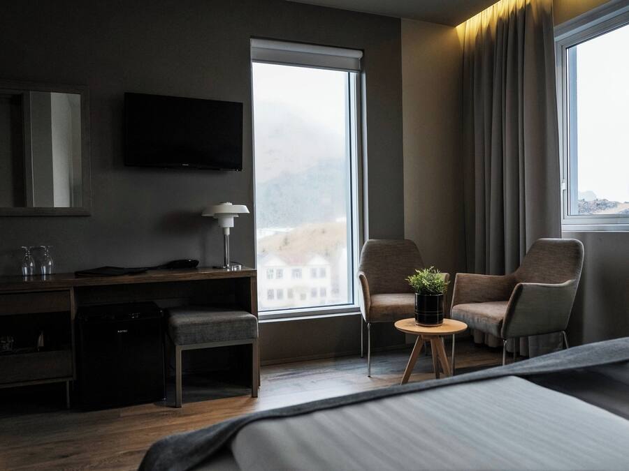 Habitación de hotel con cama, escritorio, silla, televisión y ventana con cortinas.